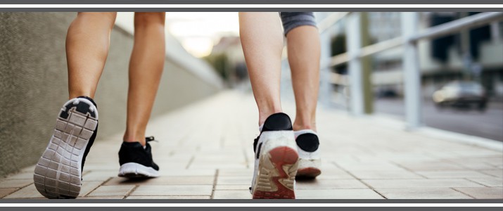 Two women on a walk showing the bottom of their shoes and the concrete.