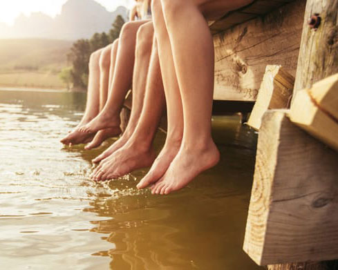 People's legs hanging over edge of dock on water